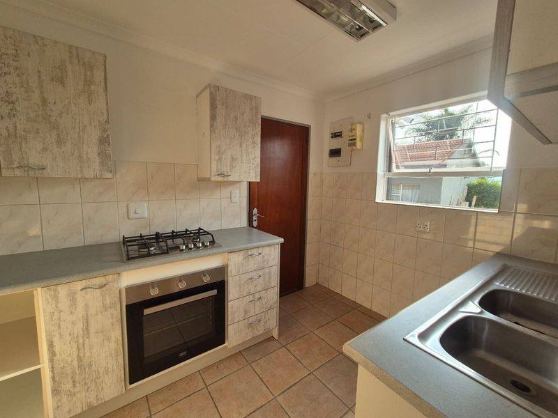 Functional kitchen featuring built-in cabinetry, gas hob, oven, double bowl sink, and tiled finishes. The space is vacant and ready for updates.
