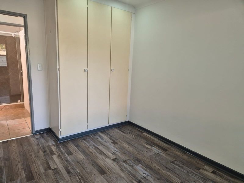 A clean, empty bedroom featuring modern laminate flooring, built-in cupboards, and direct access to an en-suite bathroom.