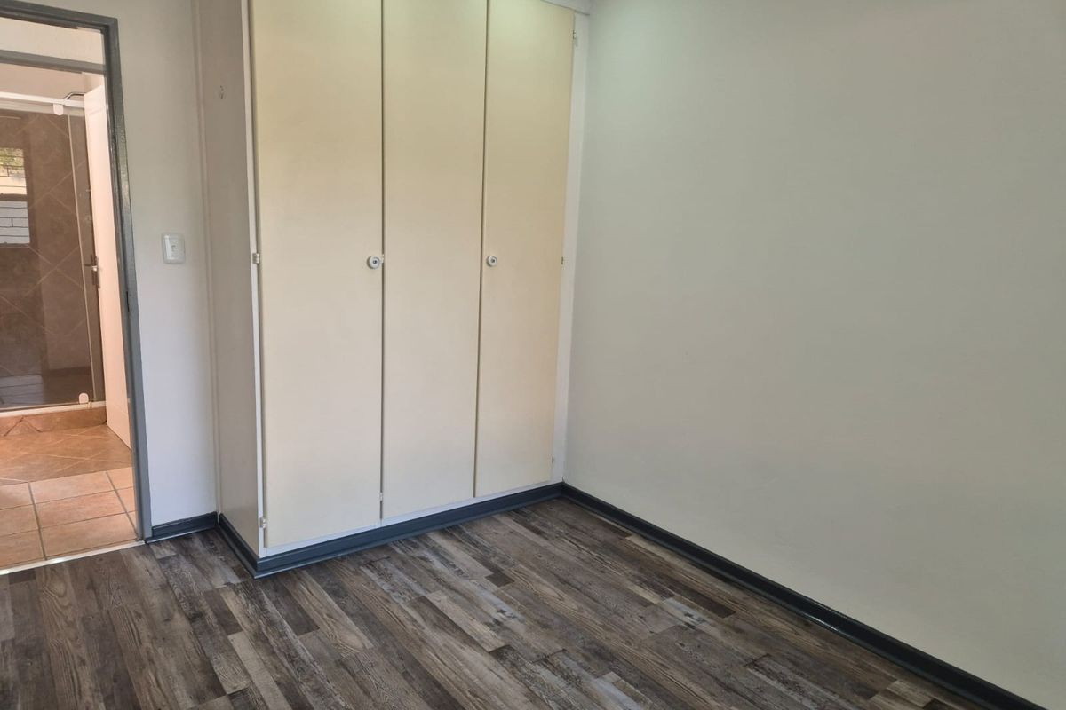 A clean, empty bedroom featuring modern laminate flooring, built-in cupboards, and direct access to an en-suite bathroom.