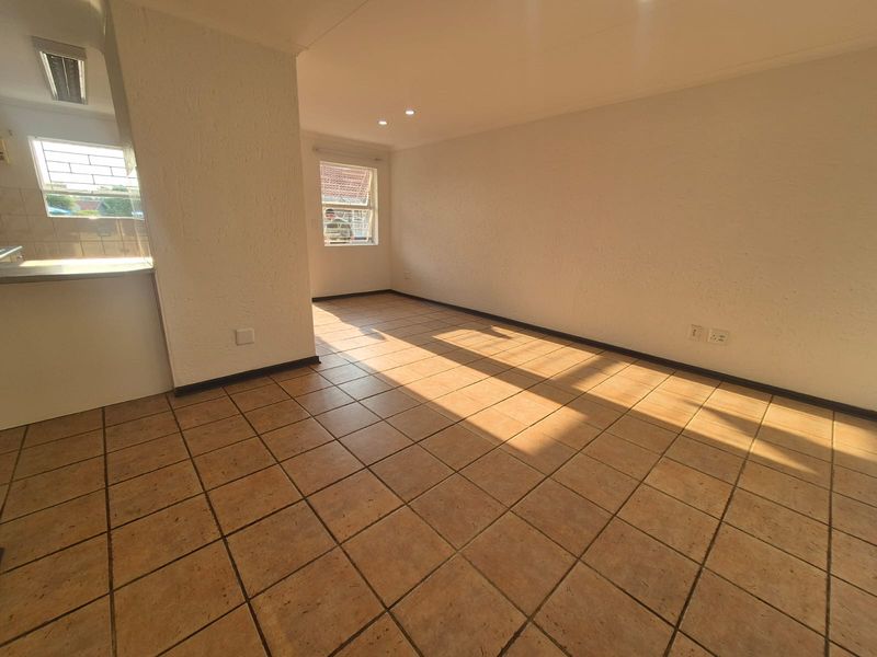 A bright, empty open-plan living area featuring tiled flooring, recessed lighting, and large windows with security bars, offering a clean canvas for personalization.