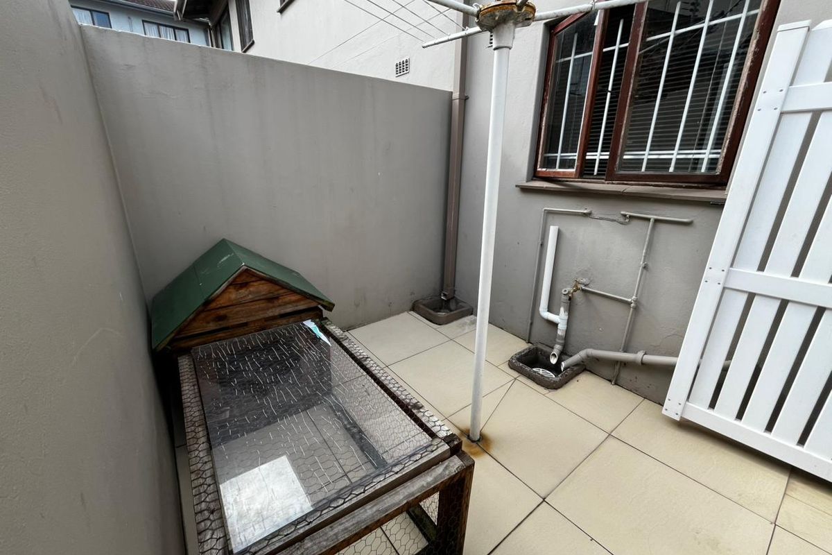 A paved rear courtyard area featuring exterior plumbing, security-barred windows, and a rotary clothesline, providing a functional outdoor utility space.