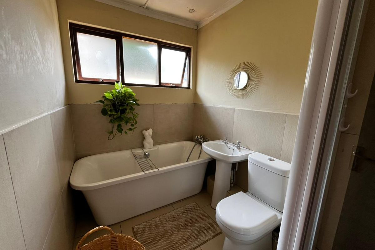 A functional bathroom featuring a freestanding bathtub, pedestal basin, and toilet, complemented by neutral wall tiling and natural light from a top-hung window.
