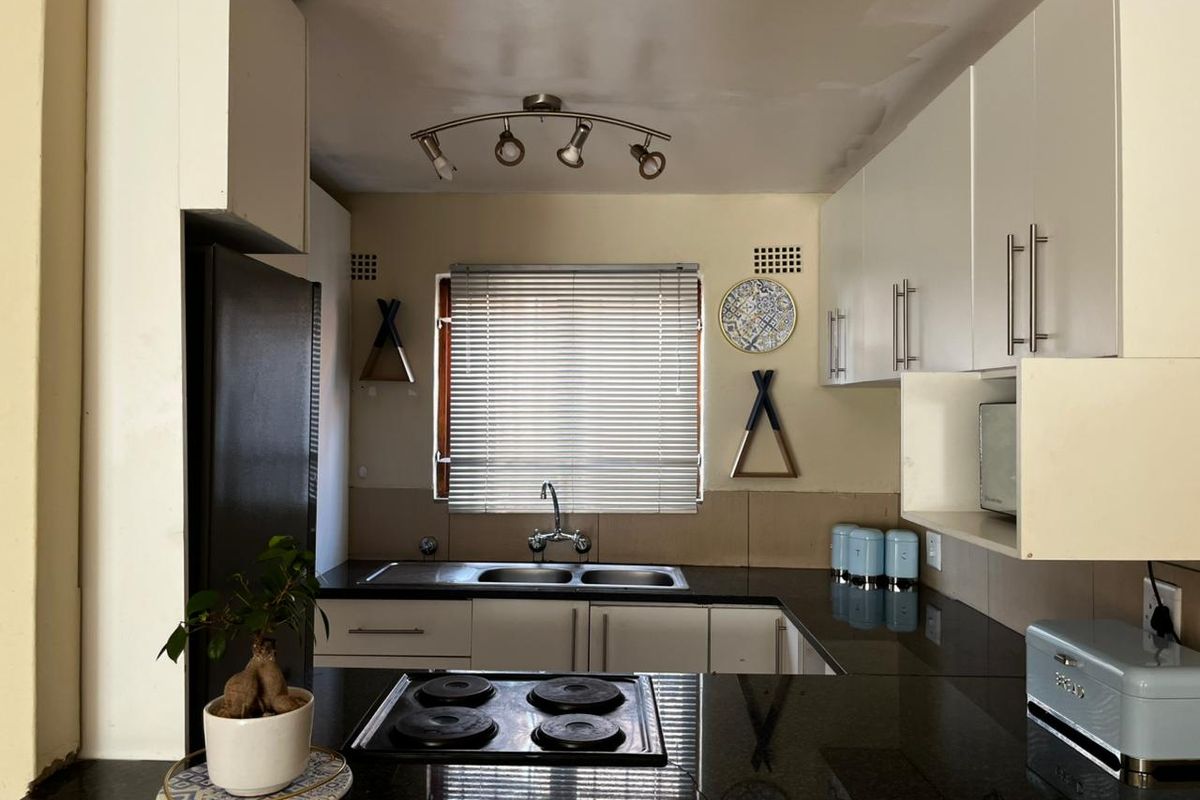 A functional kitchen featuring dark granite countertops, white cabinetry, a built-in electric hob, and a double sink with a window view.