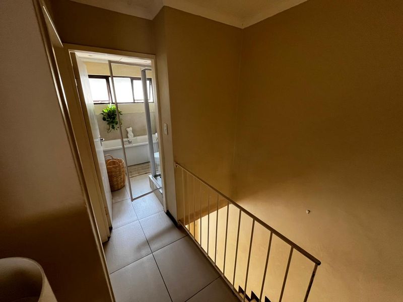 A hallway area featuring tiled flooring and a metal balustrade overlooking the staircase, with direct access to an adjacent bathroom.