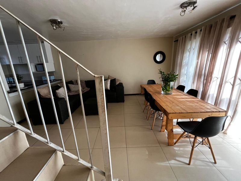 Open-plan living and dining area featuring tiled flooring, a metal staircase, and large sliding doors providing natural light.