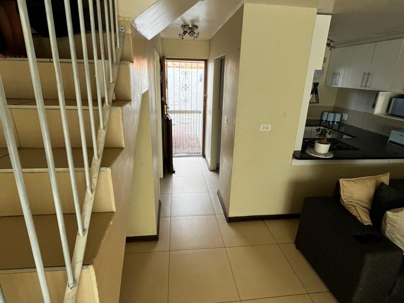 Open plan living area featuring tiled flooring, a staircase with metal balustrade, and a functional kitchen with built-in cabinetry and hob.