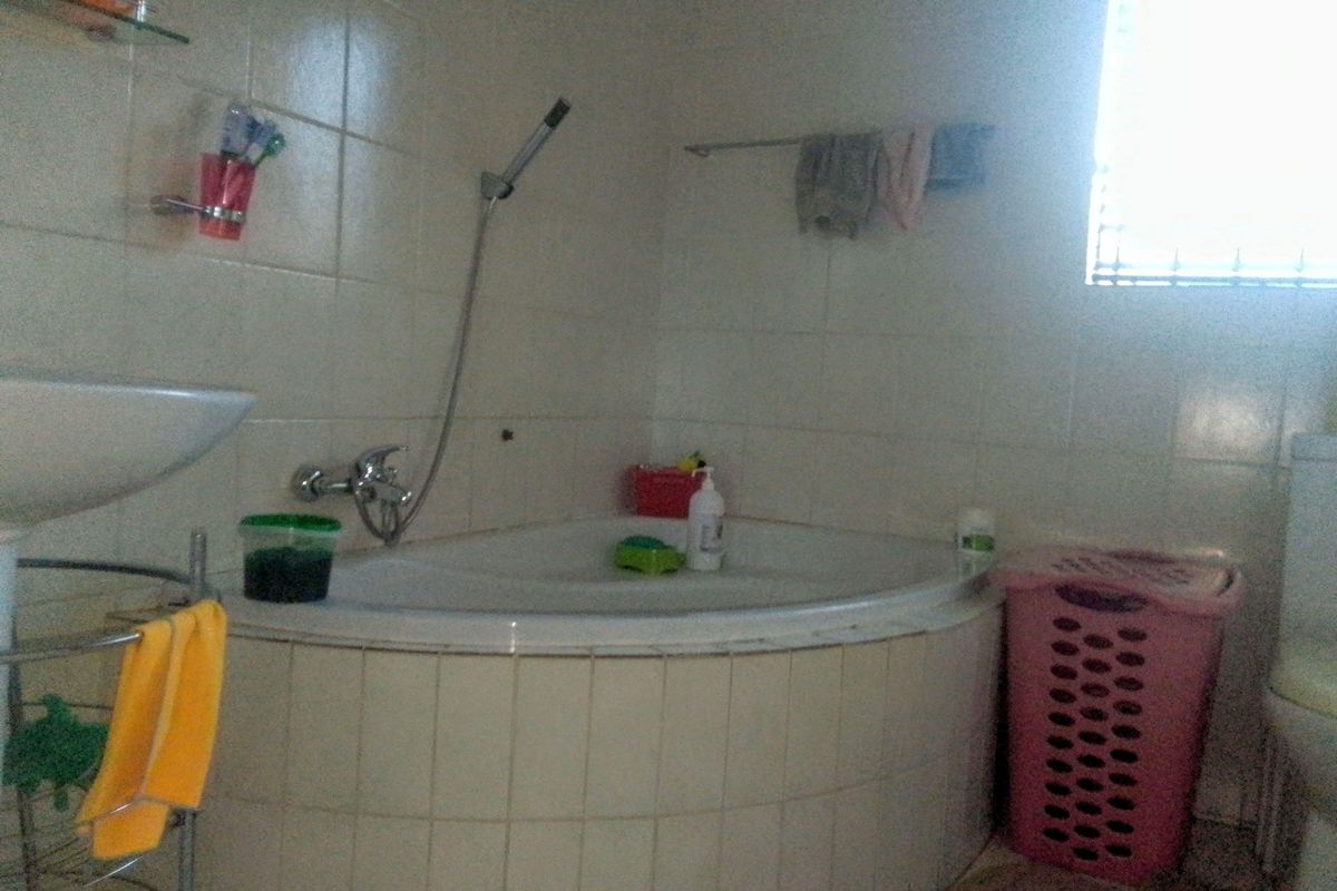 A functional bathroom featuring a corner bathtub with integrated shower mixer, wall-mounted basin, and tiled splashbacks.