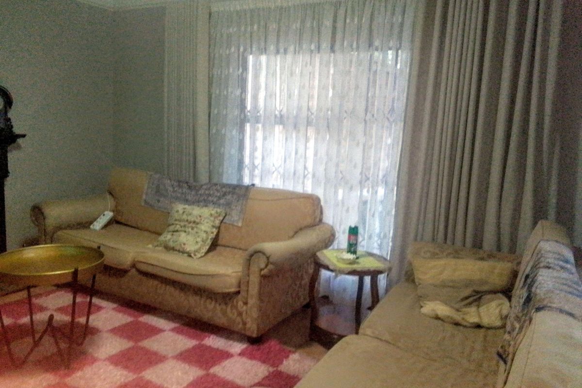 A living room featuring neutral wall tones, crown molding, and floor-to-ceiling curtains covering a large window.