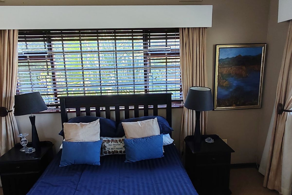 A bedroom featuring dual windows with venetian blinds, curtain pelmets, and built-in shelving, offering a functional and well-lit living space.