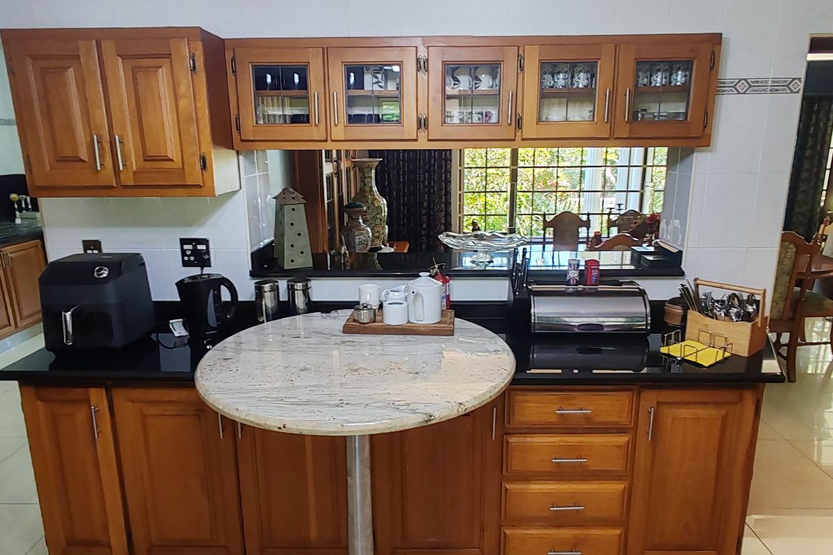 A functional kitchen featuring warm wooden cabinetry, contrasting black granite countertops, a built-in breakfast bar, and tiled flooring with a view into the dining area.