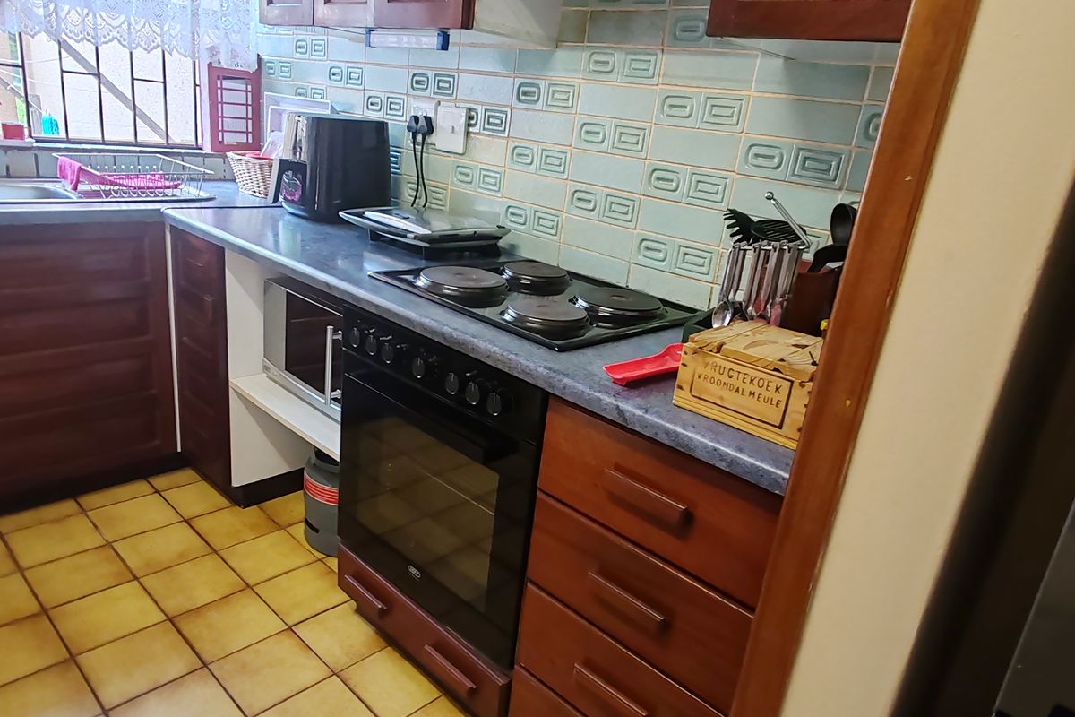 A functional kitchen featuring wooden cabinetry, a built-in oven with electric hob, tiled flooring, and a double basin sink with a window view.
