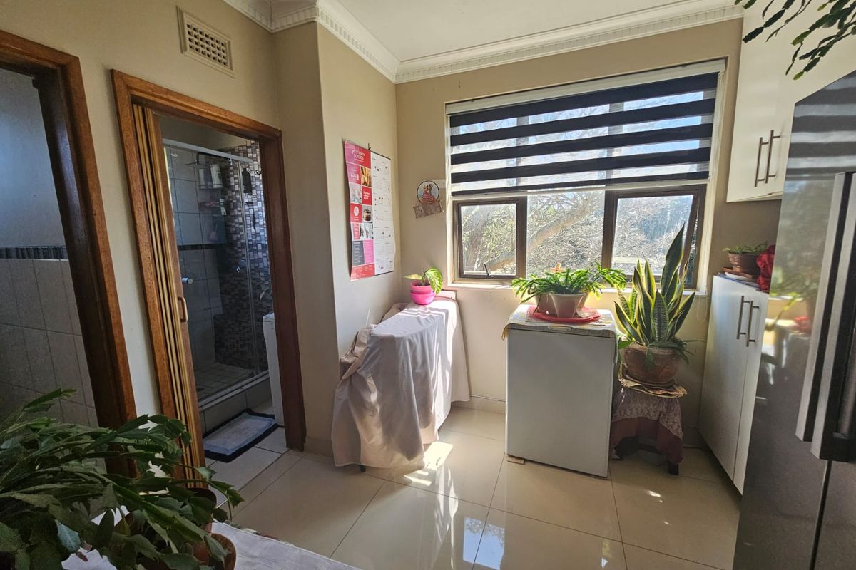 A functional kitchen area featuring tiled flooring, built-in cabinetry, and a window with fitted blinds, providing access to an adjacent bathroom.