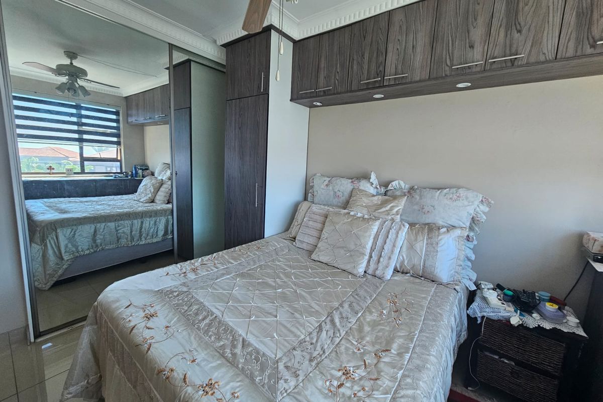 A well-maintained bedroom featuring built-in cupboards with overhead storage, mirrored wardrobe doors, and tiled flooring.