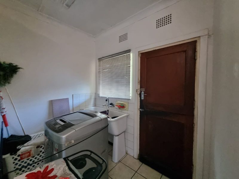 A functional laundry area featuring a utility sink, tiled flooring, and direct exterior access through a wooden door.