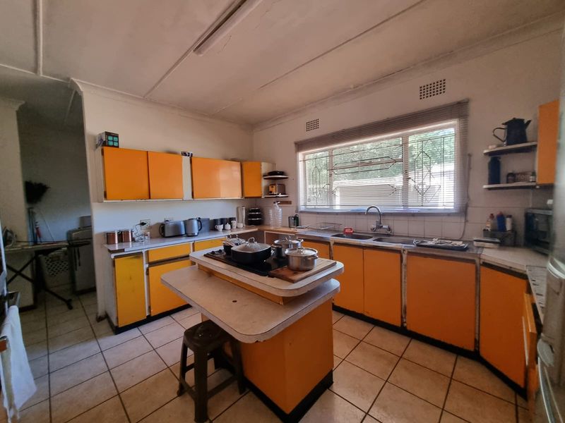 A dated kitchen featuring bright orange cabinetry, a central island with a built-in hob, double sink, and tiled flooring.