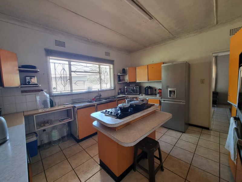 A dated kitchen featuring an island with a built-in hob, ample cabinetry, and tiled flooring, offering significant potential for a modern renovation.