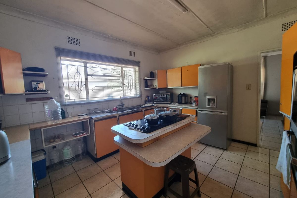 A dated kitchen featuring an island with a built-in hob, ample cabinetry, and tiled flooring, offering significant potential for a modern renovation.