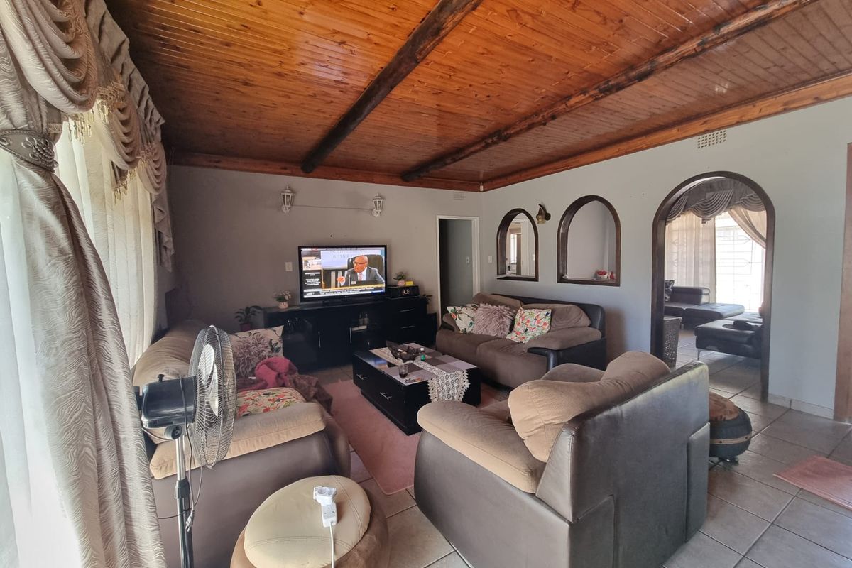 A spacious living room featuring a warm timber-clad ceiling with exposed beams, ceramic tiled flooring, and decorative arched wall niches.