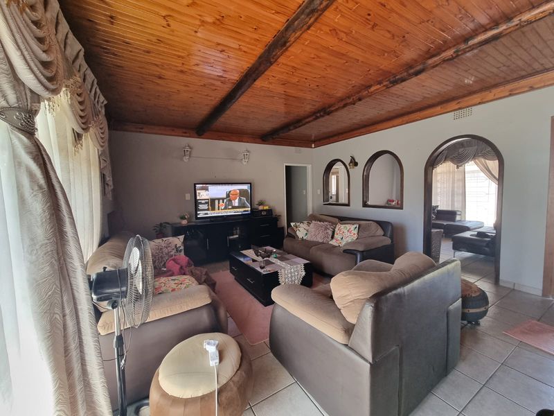 A spacious living room featuring a warm timber-clad ceiling with exposed beams, ceramic tiled flooring, and decorative arched wall niches.
