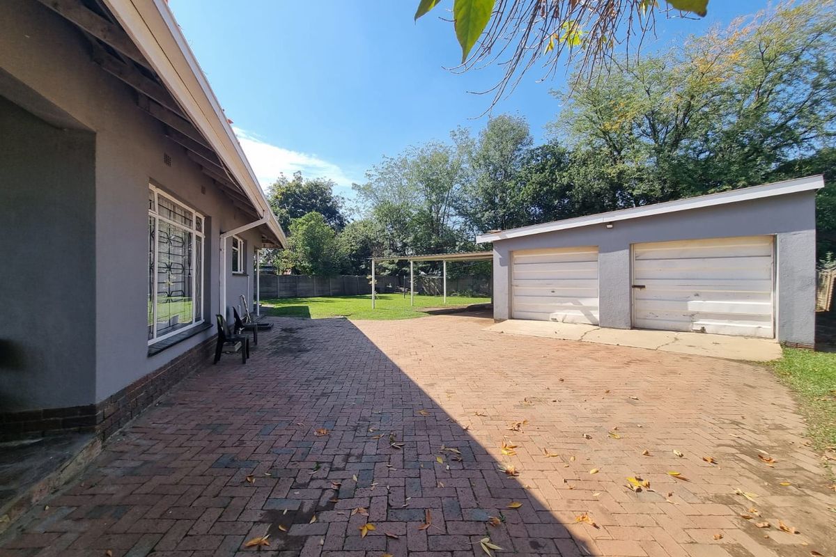 Rear exterior view featuring a brick paved driveway, double garage with metal doors, and a spacious backyard area.