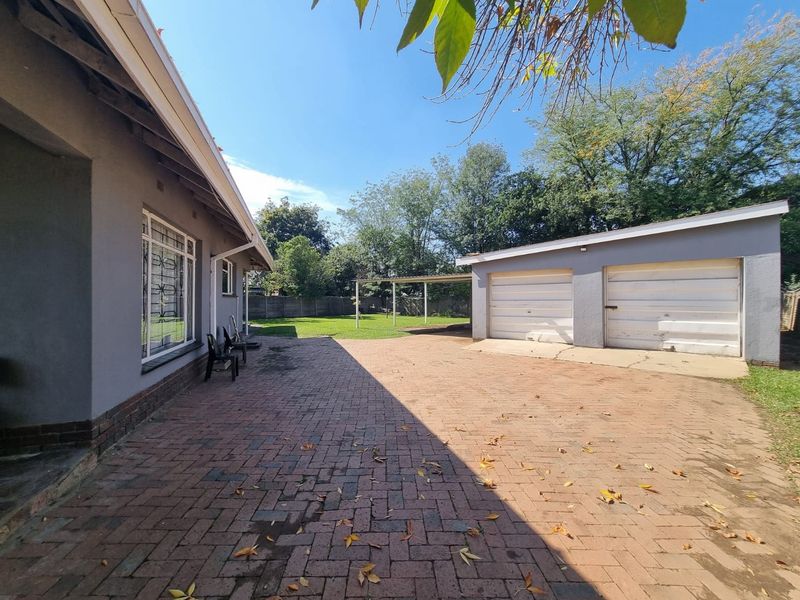 Rear exterior view featuring a brick paved driveway, double garage with metal doors, and a spacious backyard area.