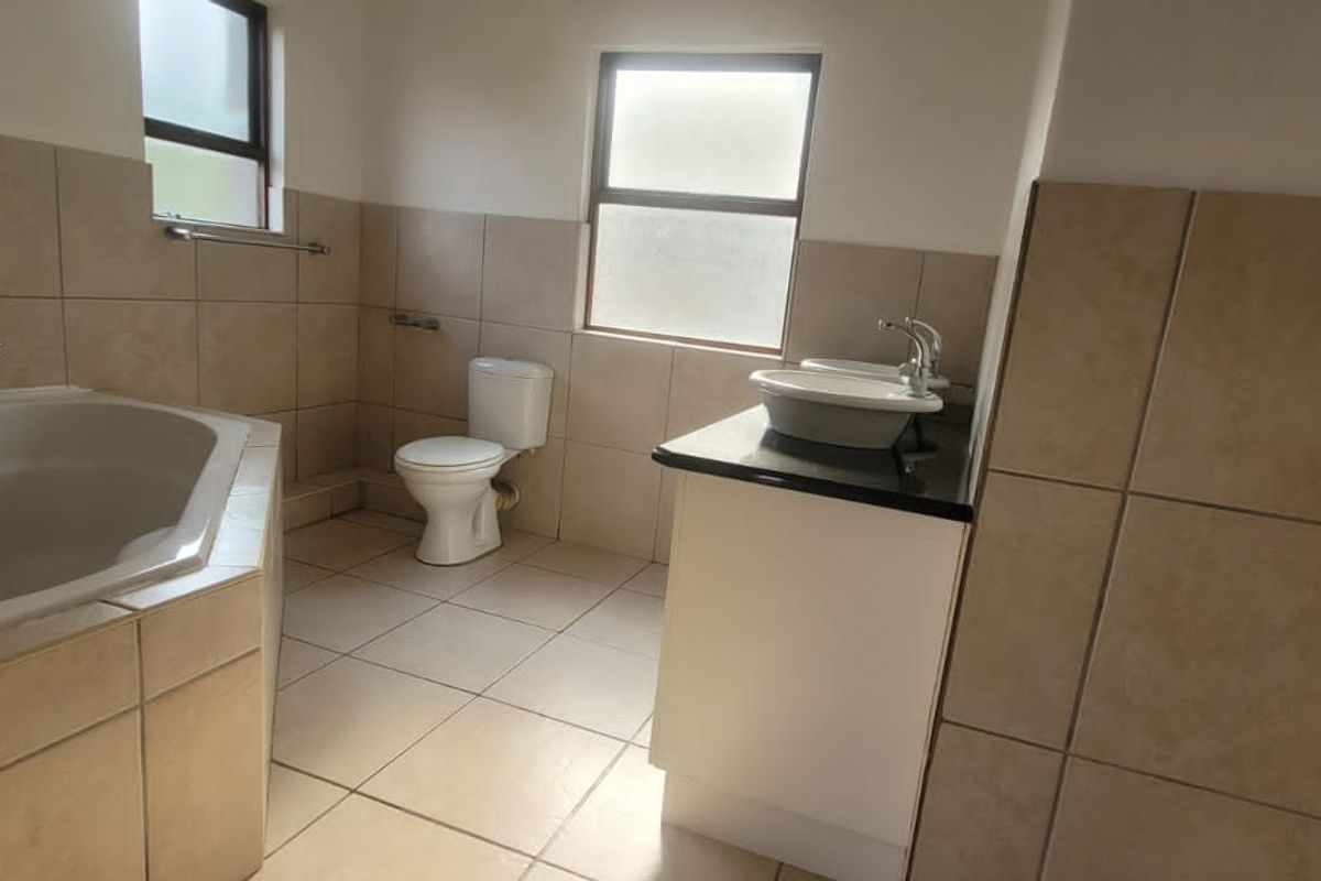 A functional bathroom featuring a corner bathtub, a toilet, and a vanity with a vessel sink, finished with neutral wall and floor tiling.