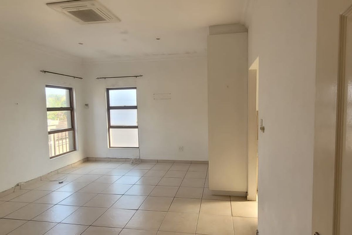 A spacious, empty living area featuring tiled flooring, recessed ceiling lighting, and large windows that provide ample natural light.
