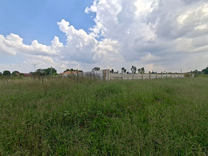 A vacant residential plot featuring overgrown grass and a precast concrete boundary wall, offering a blank canvas for future development.
