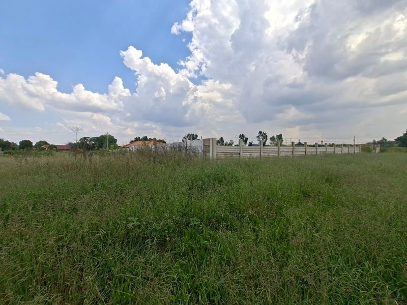 A vacant residential plot featuring overgrown grass and a precast concrete boundary wall, offering a blank canvas for future development.