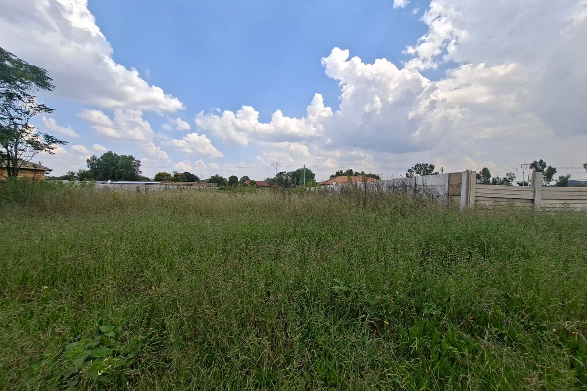 A vacant residential plot featuring overgrown grass and a precast concrete boundary wall, offering a blank canvas for future development.
