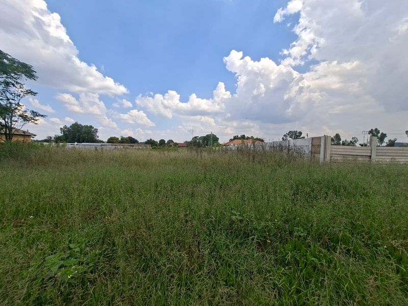 A vacant residential plot featuring overgrown grass and a precast concrete boundary wall, offering a blank canvas for future development.