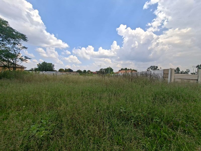 A vacant residential plot featuring overgrown grass and a precast concrete boundary wall, offering a clear space for future development.