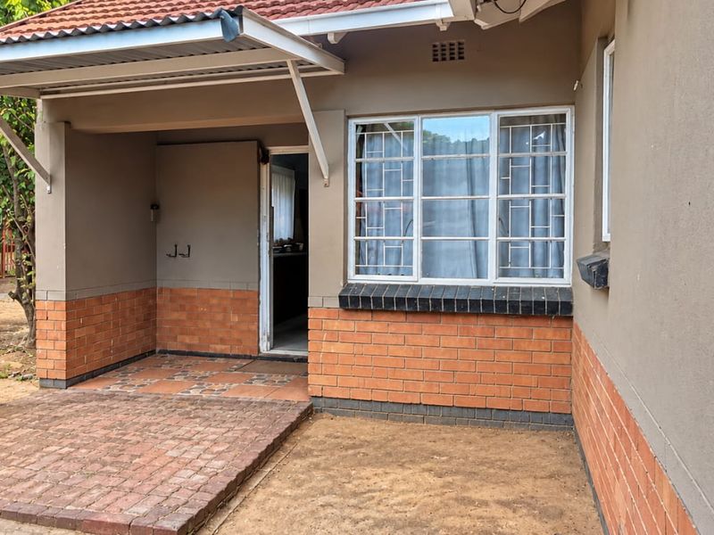 Front entrance area featuring a brick facade, tiled patio, and security bars on the windows.