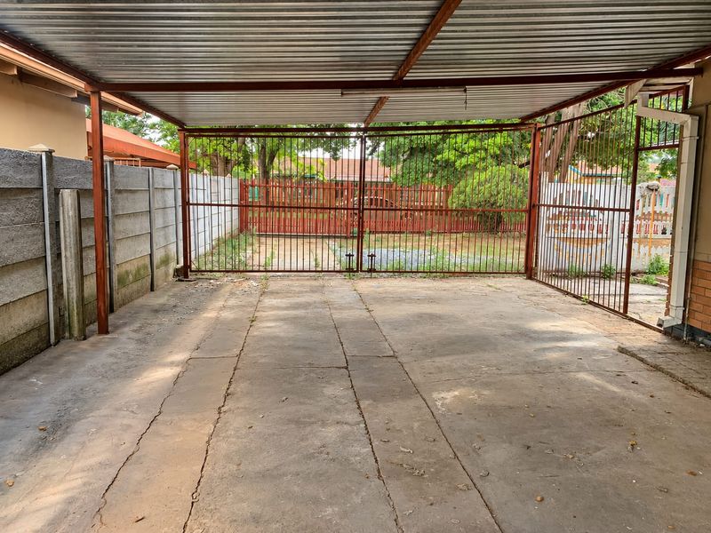 A covered carport area featuring a corrugated metal roof, concrete flooring, and a secure steel gate entrance.