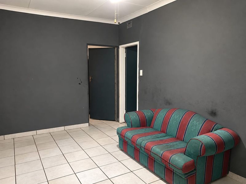 A living room featuring ceramic floor tiles and dark painted walls, requiring cosmetic updates to address wall scuffs and marks.
