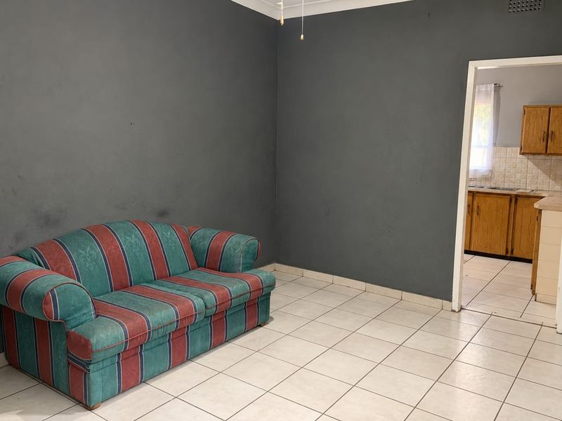 A living room featuring tiled flooring and dark grey walls, with a doorway leading through to a kitchen area.