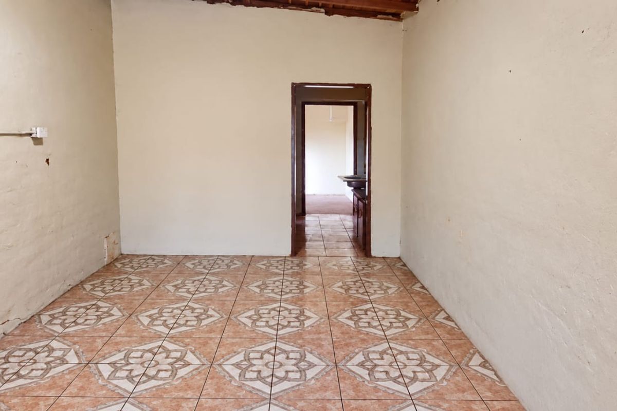 An empty living room featuring patterned ceramic floor tiles and exposed timber ceiling beams, requiring cosmetic updates and wall repairs.