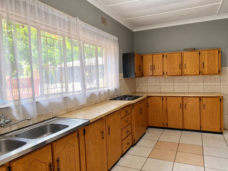 A functional kitchen featuring wooden cabinetry, laminate countertops, a built-in gas hob, and tiled flooring, offering a classic layout ready for modernization.