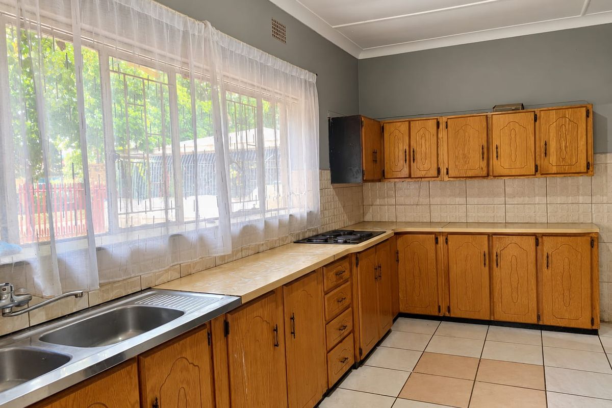 A functional kitchen featuring wooden cabinetry, laminate countertops, a built-in gas hob, and tiled flooring, offering a classic layout ready for modernization.