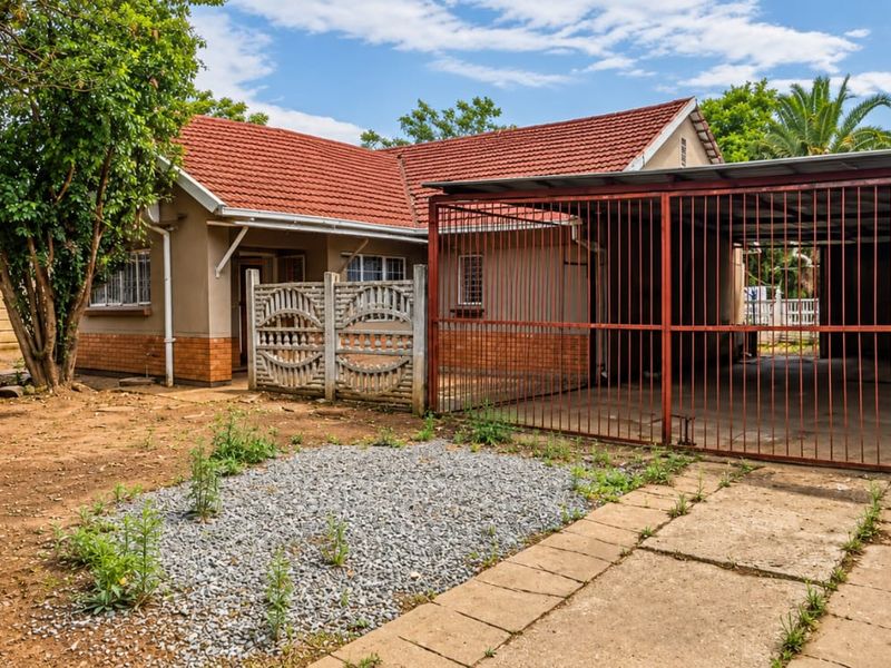 Front view of a single-story house featuring a tiled roof, brick accents, and an attached metal carport with a secure gated entrance.
