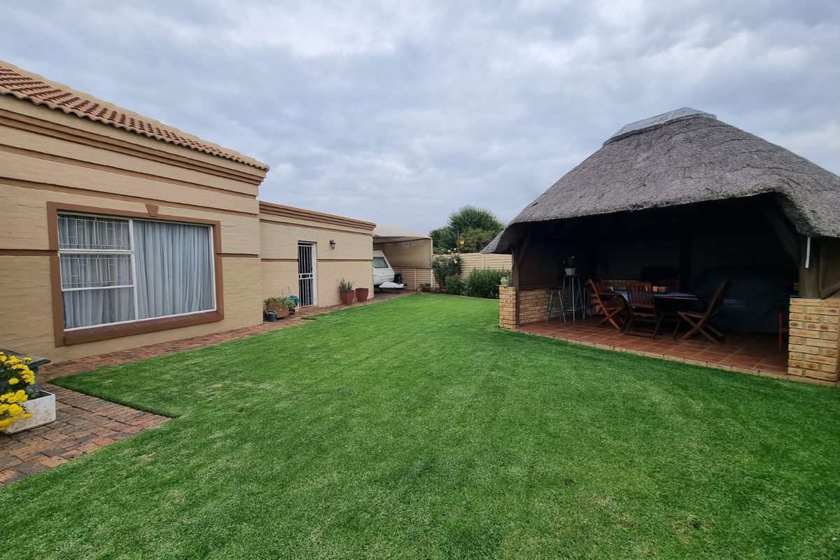 A well-maintained rear garden featuring a spacious lawn, brick-paved areas, and a traditional thatched lapa for outdoor entertainment.