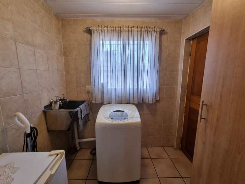 A functional laundry room featuring tiled walls and flooring, equipped with a stainless steel utility sink and space for laundry appliances.