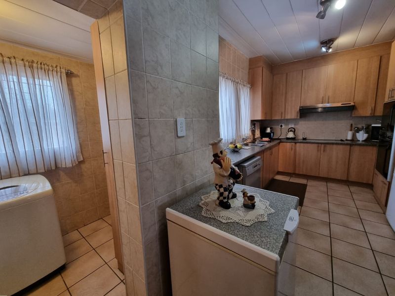 Open plan kitchen and laundry area featuring tiled flooring, built-in wooden cabinetry, and a tiled partition wall.