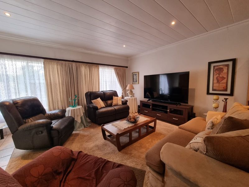 A comfortable living room featuring a tongue and groove ceiling with recessed lighting and large windows dressed with curtains.