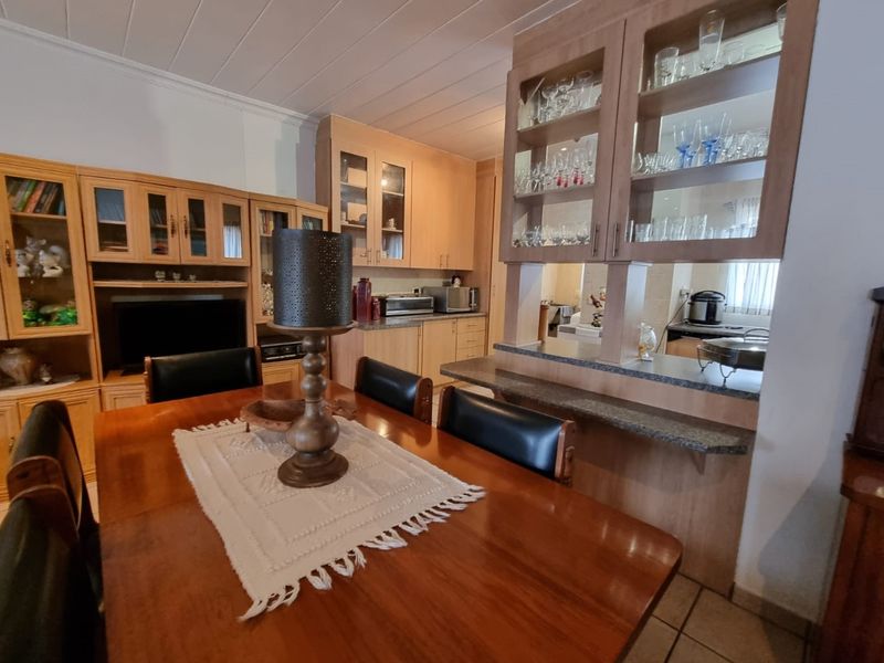 Open plan dining and kitchen area featuring wooden cabinetry, a breakfast bar, and glass-fronted display units, creating a functional and connected living space.