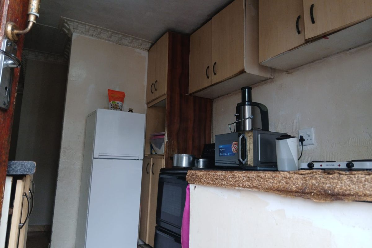 A compact kitchen featuring built-in cabinetry and a stove, currently showing significant signs of wear and requiring cosmetic updates.