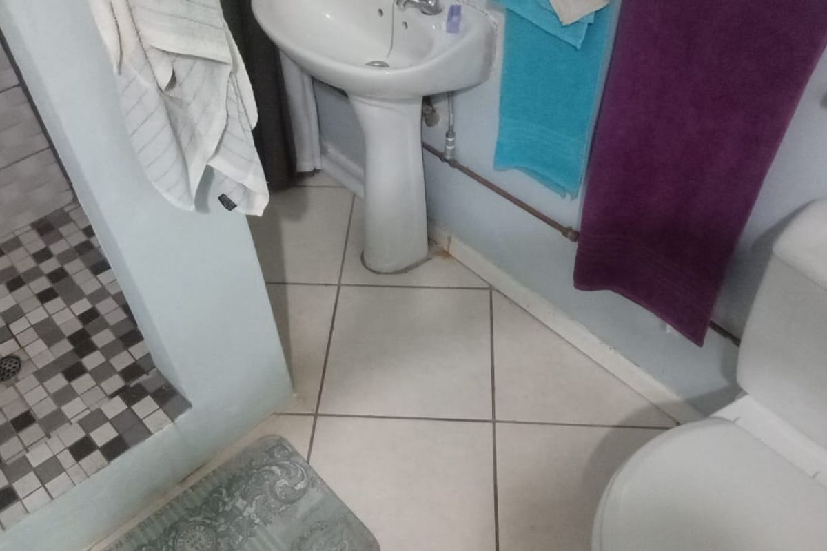 A functional bathroom featuring a pedestal sink, a tiled shower enclosure with mosaic accents, and a standard toilet.