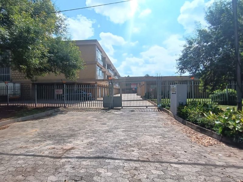 Front entrance view of a multi-story brick apartment complex featuring a secure gated driveway and perimeter fencing.
