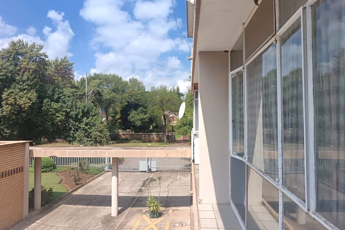 An elevated view of the property exterior featuring a tiled balcony overlooking a concrete driveway, covered walkway, and secure gated entrance.