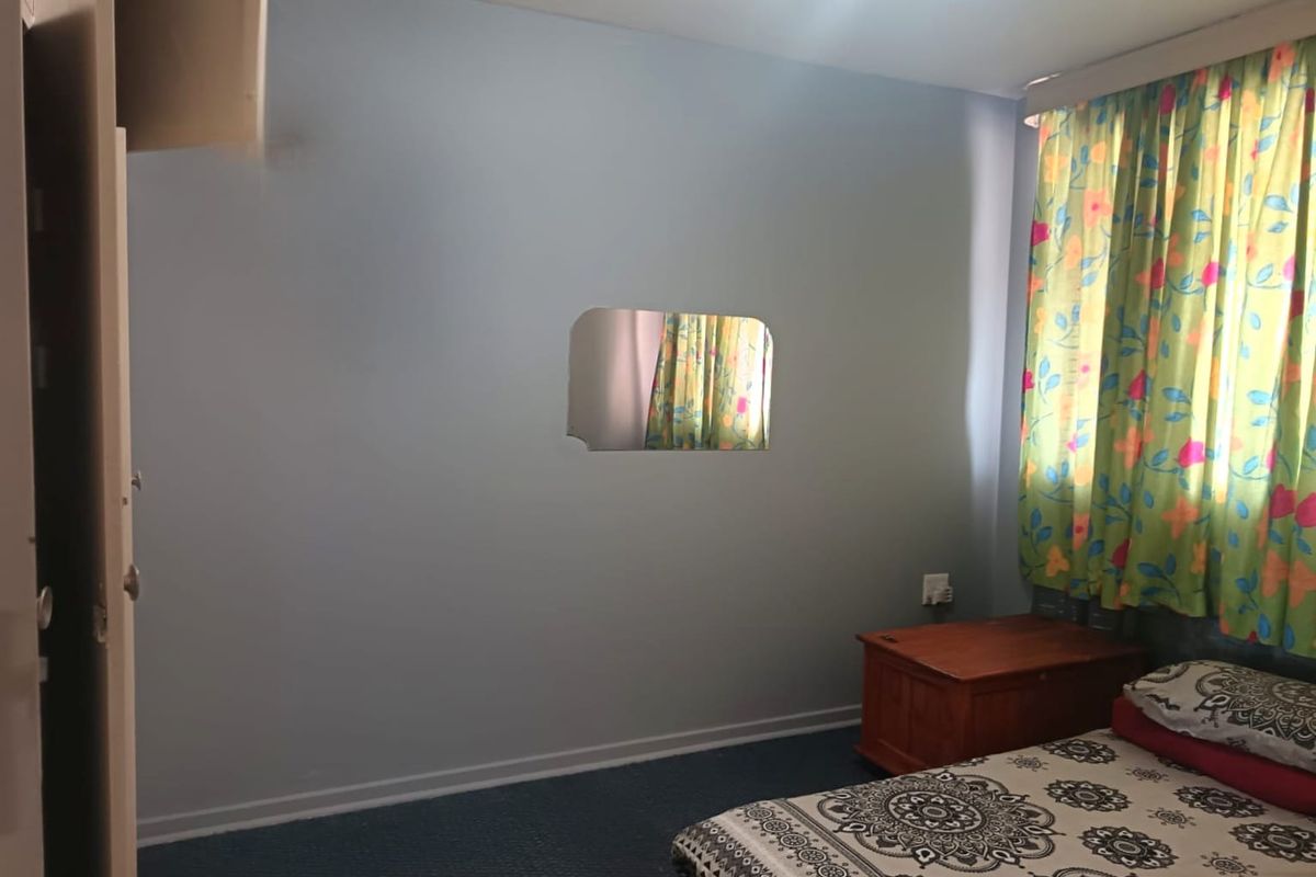 A bedroom featuring blue walls, carpeted flooring, and a built-in cupboard, offering a functional space ready for personalization.